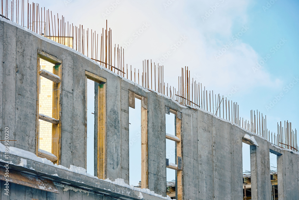 Сonstruction site with unfinished concrete walls and exposed reinforcement bars, architectural engineering in snowy conditions. Concrete building structure with visible rebar framework