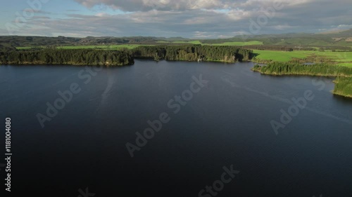 Aerial view of a still lake near Mangakino, New Zealand, with pristine waters reflecting lush greenery and forests along its tranquil shores. photo