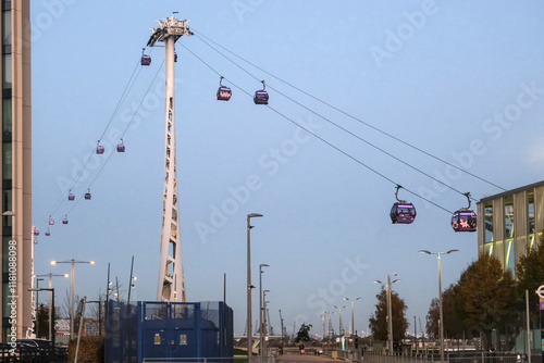 The London Cable Car (Emirates Air Line) gondolas traveling between tall towers over a city street, capturing urban transport innovation near the Thames. photo