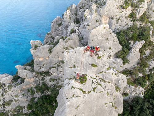 Aerial view of climbers scaling the rugged guglia di goloritze with beautiful blue water and scenic coastline, Baunei, Italy. photo