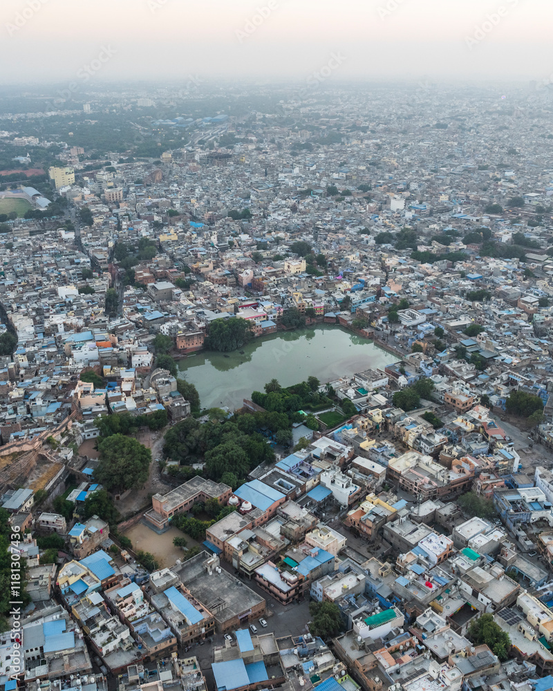 Aerial view of densely populated cityscape with rooftops and greenery surrounding a lake, Sri Ganganagar, India. Aerial view of densely populated cityscape with rooftops and greenery surrounding a lake, Sri Ganganagar, India.