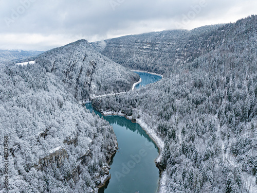 Aerial view of snowy landscape in the valley of River Doubs surrounded by majestic mountains and tranquil forests, Les Brenets, Switzerland.