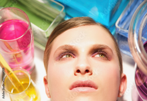 Close up of a young woman face surrounded by chemical glassware
