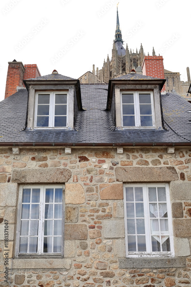 Fototapeta premium Mont-Saint-Michel= Le Montoise medieval building rear facade, seen under the abbey bell tower and spire from the rampart walkway. Normandy-France-167