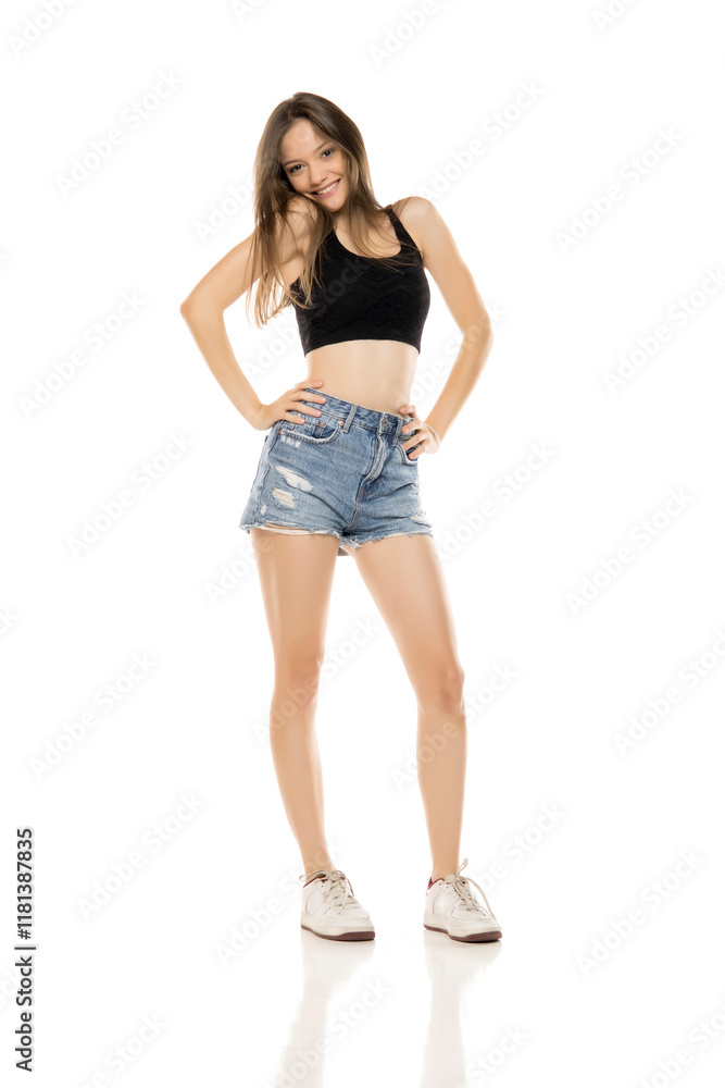 Beautiful young happy woman in a short blue jeans and black sleeveless shirt on a white studio background. Front view. Beautiful young happy woman in a short blue jeans and black sleeveless shirt on a white studio background. Front view.