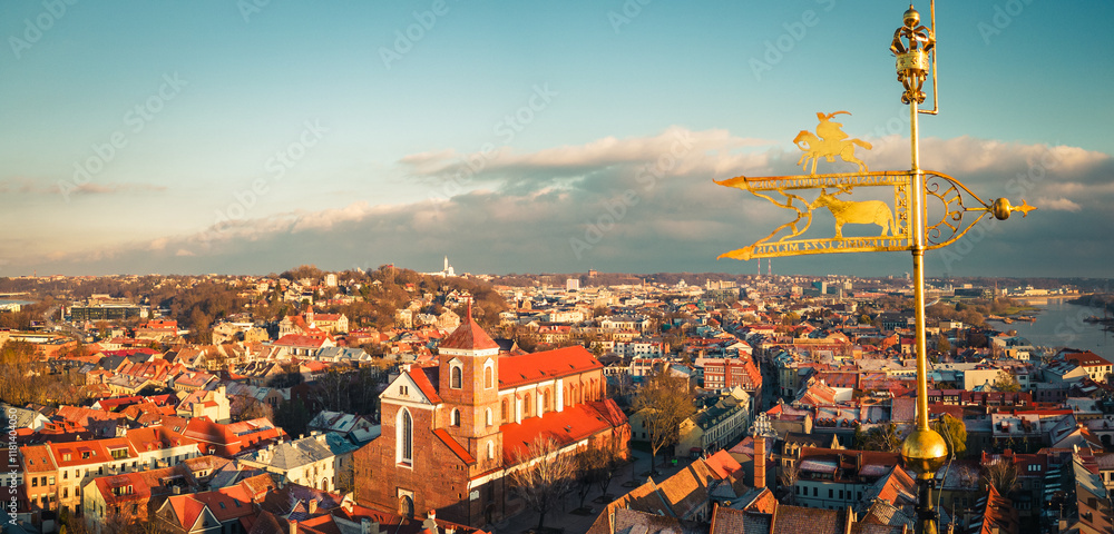 Fototapeta premium Kaunas, Lithuania - 19th november, 2024: aerial view beautiful metal artwork golden plate on top of town hall tower. Cathedral-Basilica of St. Peter and St. Paul and Kaunas cityscape 4k panorama