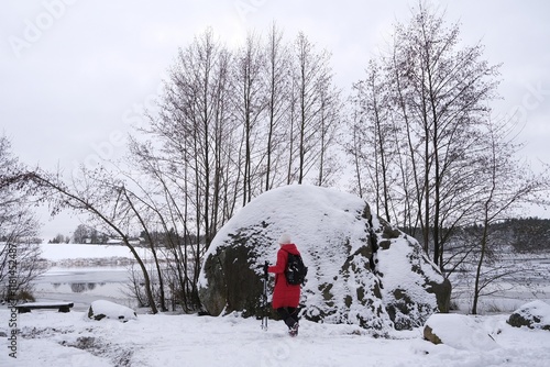 Huge Devil Stone by Kamienne Lake and silhouette of woman in red coat in winter scenery. Zurawie Blota (Mud Cranes)  Nature Reserve, Kashubian Landscape Park, Mirachowskie Forests, Pomerania, Poland. photo