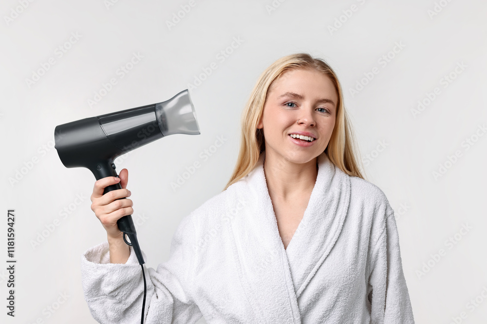 Beautiful young woman drying her hair with hairdryer on light grey background Beautiful young woman drying her hair with hairdryer on light grey background