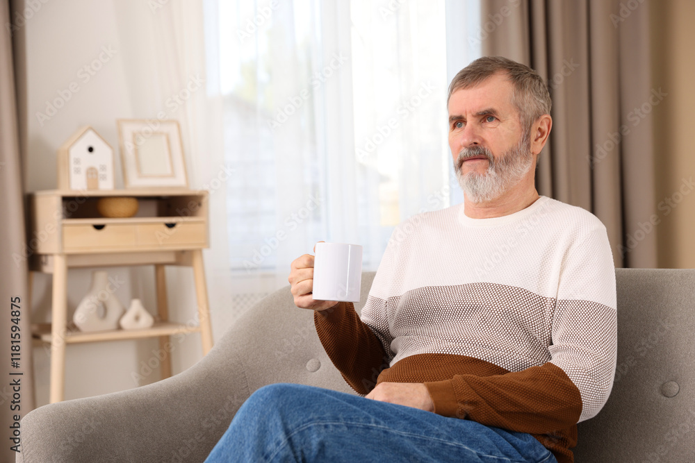 Mature man with cup of hot drink on sofa at home. Space for text Mature man with cup of hot drink on sofa at home. Space for text