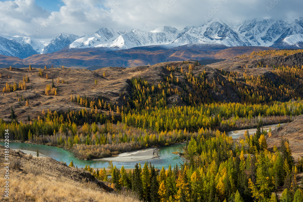 Fototapeta premium Beautiful autumn landscape featuring vibrant trees, a meandering river, and snowy mountains. Capturing peaceful seasonal scenery under a partially cloudy sky with vivid contrasts of colors.