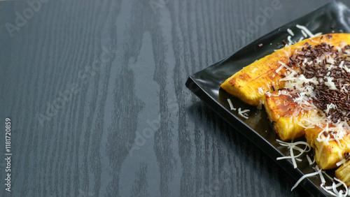 a plate of Pisang Goreng Keju Coklat, a popular Indonesian dessert. Slices of fried banana are generously sprinkled with grated cheese and chocolate chips photo