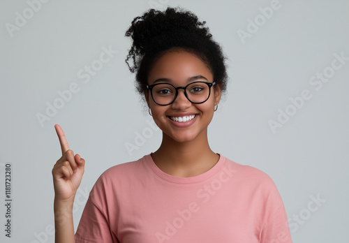 Portrait of a happy young woman wearing glasses, smiling and pointing her finger upward, isolated on a white background. 