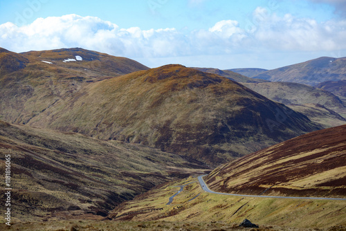 Scenic view of rolling hills and winding road in the Scottish Highlands under a clear blue sky