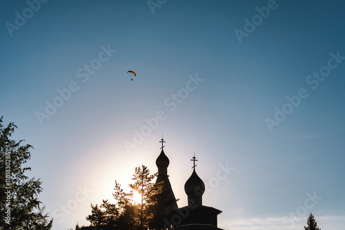 A parachutist flying over a cathedral in the evening