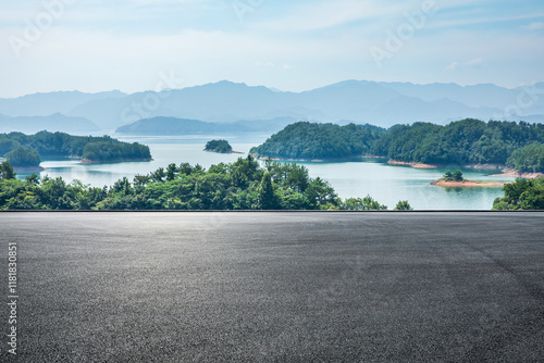 Fototapeta Naklejka Na Ścianę i Meble -  Asphalt road square and lake water with green mountain nature landscape under blue sky. Outdoor asphalt parking lot.