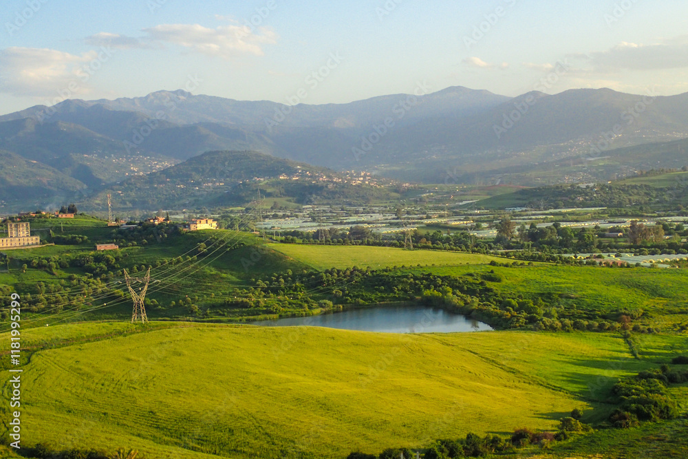 Naklejka premium African countryside, Spring day landscape of fields, meadows and hills with mountains in the background and blue sky with clouds, Algerian and a lake in the Algerian countryside, rural Jijel Algeria.