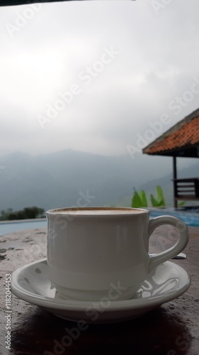 A cup of coffe ona table with a view of pool and mountain