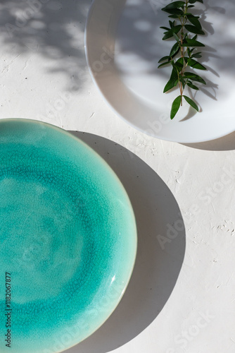 Empty turquoise ceramic plate on white plaster background with myrtle leaves shadows. Spring or summer table setting.