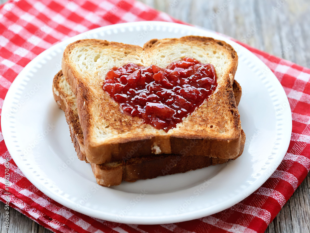 Heart-shaped toast with jelly on a white plate placed on a checkered tablecloth. Valentine’s Day idea, date, engagement party, love party, eat, food Heart-shaped toast with jelly on a white plate placed on a checkered tablecloth. Valentine’s Day idea, date, engagement party, love party, eat, food