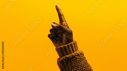  hand pointing upwards, wearing a textured sweater, set against a solid, minimal background with vibrant yellow tones. The image conveys a sense of direction, creativity, and clarity.   photo