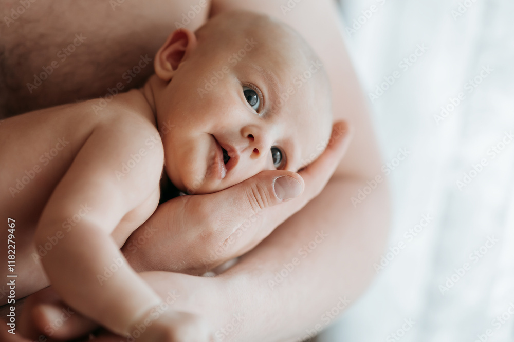 A baby is being held by a parent, with its eyes closed and a smile on its face. The baby is wrapped in a blanket, and its tiny fingers are curled around the parent's hand A baby is being held by a parent, with its eyes closed and a smile on its face. The baby is wrapped in a blanket, and its tiny fingers are curled around the parent's hand