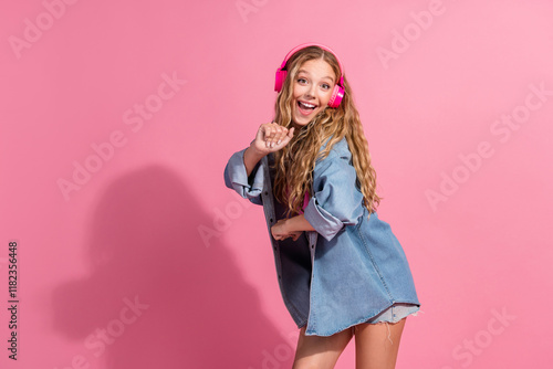 Stylish young woman in denim enjoying music with pink headphones on a vibrant backdrop photo