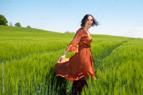 Wallpaper Mural Joyful young caucasian woman in orange dress spinning in lush green field Torontodigital.ca