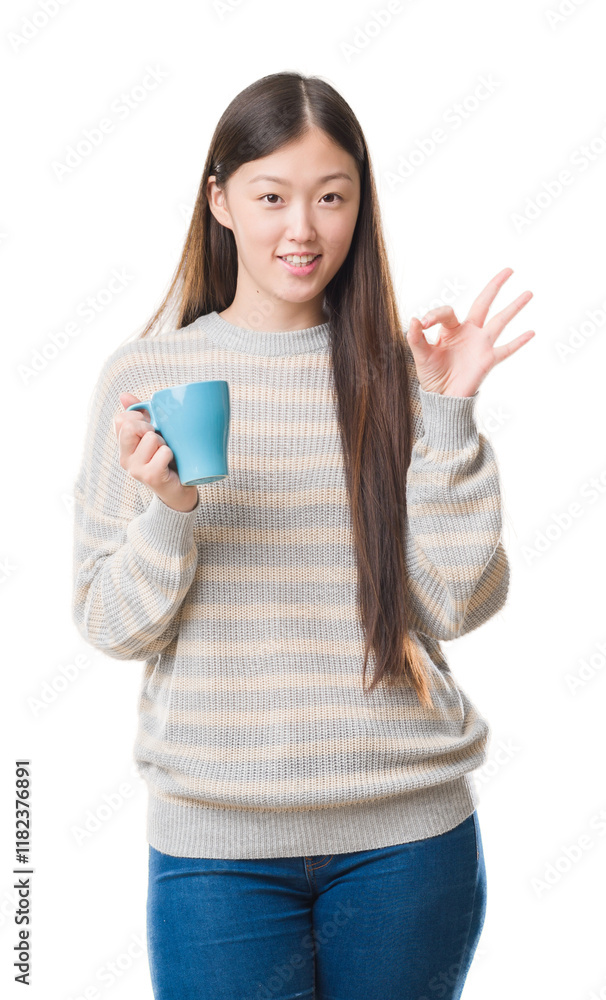 Young Chinese woman over isolated background driking cup of coffee doing ok sign with fingers, excellent symbol Young Chinese woman over isolated background driking cup of coffee doing ok sign with fingers, excellent symbol