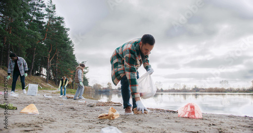 Schilderij op canvas Small group of people picking up pieces of garbage littered on beach of big lake