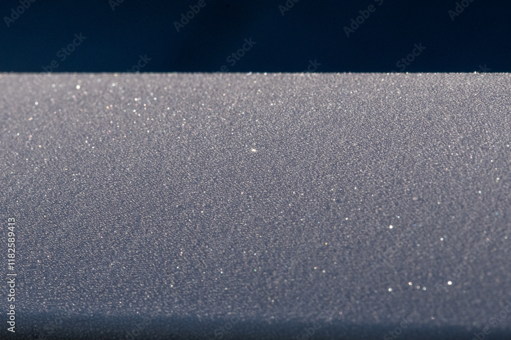 Fototapeta premium A metal railing covered in a small textured pattern of frost crystals. The frozen water has formed frosted particles of ice, cool icy crystals of frosted sleet and snowy diamond sparkles.
