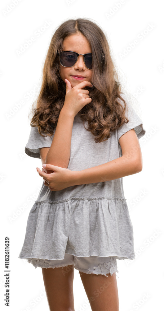 Brunette hispanic girl wearing sunglasses looking confident at the camera with smile with crossed arms and hand raised on chin. Thinking positive. Brunette hispanic girl wearing sunglasses looking confident at the camera with smile with crossed arms and hand raised on chin. Thinking positive.