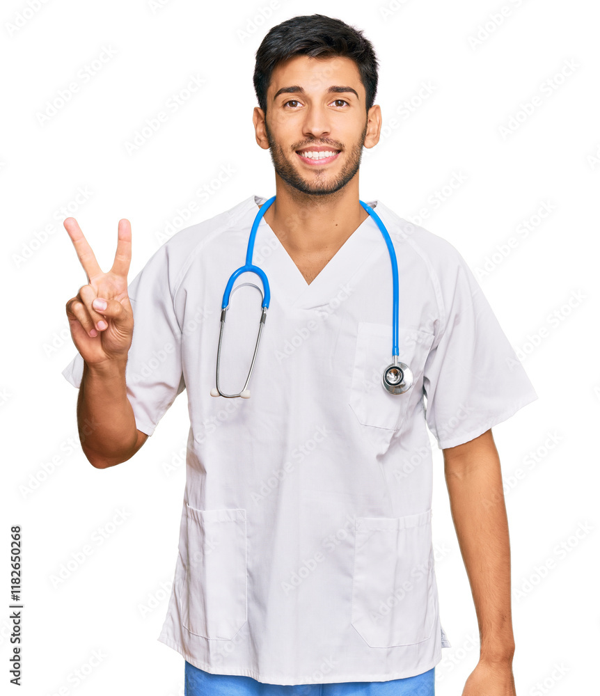 Young handsome man wearing doctor uniform and stethoscope smiling with happy face winking at the camera doing victory sign. number two. Young handsome man wearing doctor uniform and stethoscope smiling with happy face winking at the camera doing victory sign. number two.