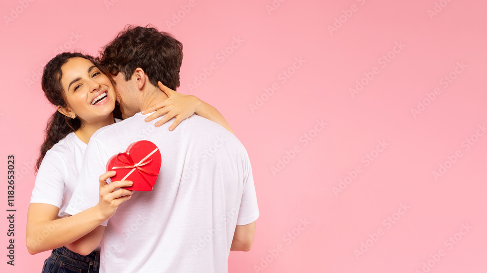 Happy European couple hugging, lady holding heart shaped gift box and embracing her man, celebrating Valentine's Day on pink background, free space, banner Happy European couple hugging, lady holding heart shaped gift box and embracing her man, celebrating Valentine's Day on pink background, free space, banner