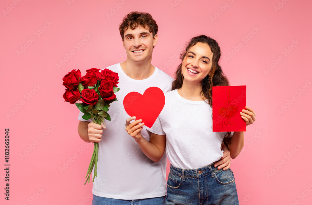 Happy European couple posing with bouquet of flowers, red paper heart-shaped and card with I love you, posing on pink background. Valentine's Day concept Happy European couple posing with bouquet of flowers, red paper heart-shaped and card with I love you, posing on pink background. Valentine's Day concept