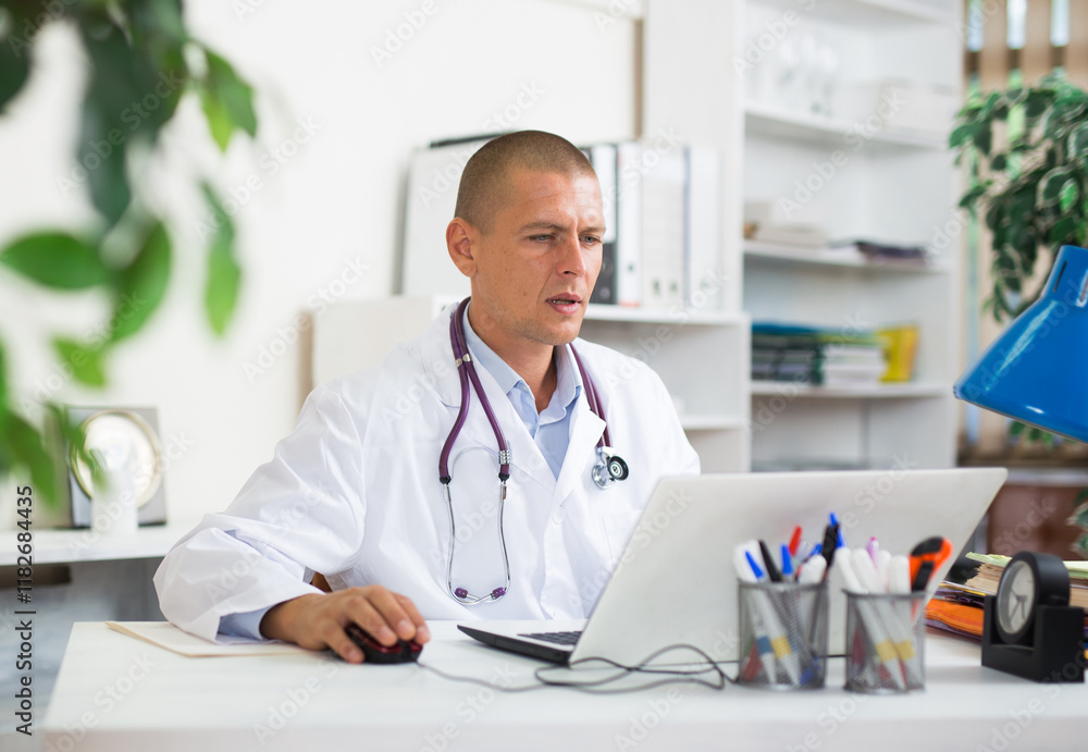 Focused man doctor working in medical office using laptop computer Focused man doctor working in medical office using laptop computer