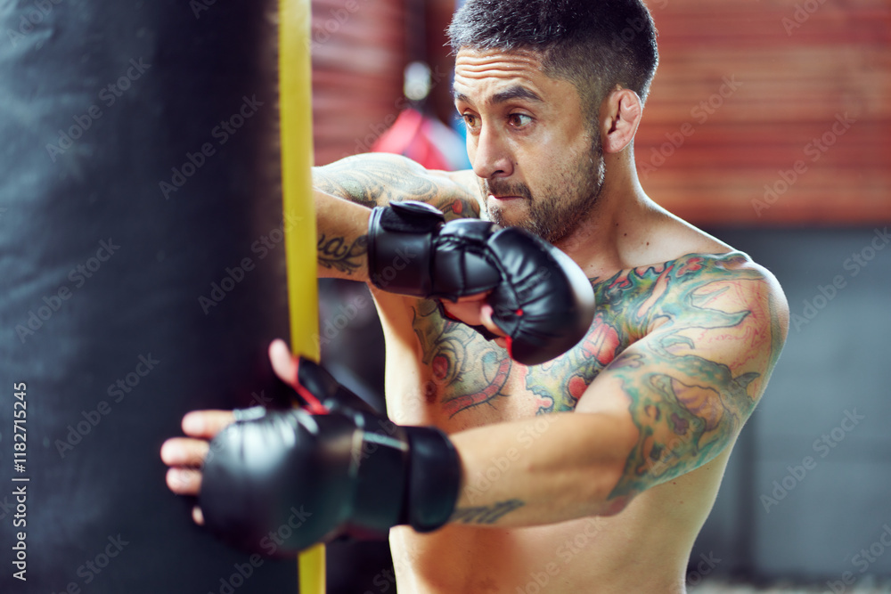 Naklejka premium Male boxer wearing boxing gloves training with punching bag, practicing powerful punches in gym