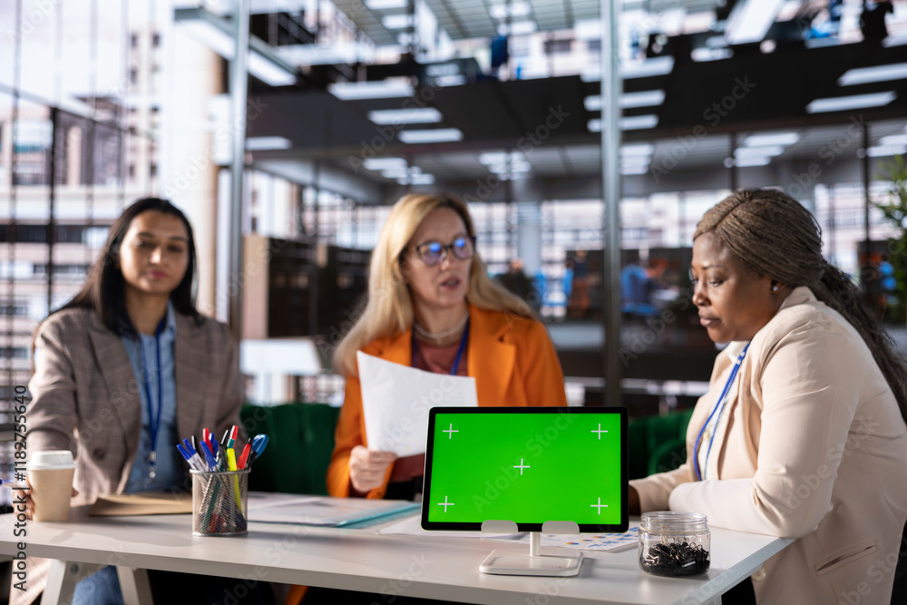 Fototapeta premium Diverse group of female colleagues ensuring goals achievement next to chroma key display, believing in equal rights and women empowerment. Powerful businesswomen work with resilience.