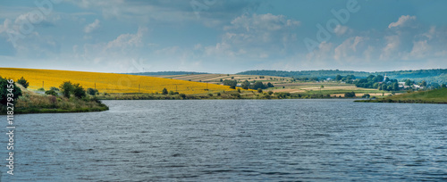 A panoramic view of a reservoir, hills with fields of sunflowers and lush gre...