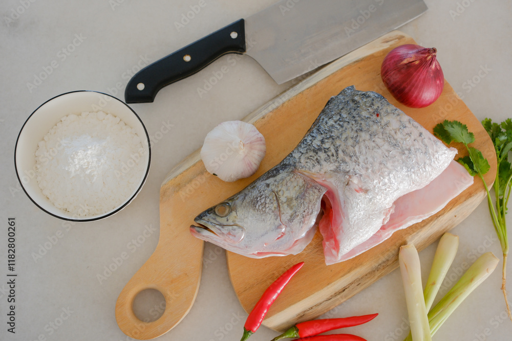 Fresh snapper fish on a wooden cutting board in a kitchen with a knife nearby