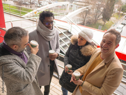 Four office workers on a coffee break in a busy business district. One Black male, a woman, and two Hispanic individuals are standing together. Only one of them, a Hispanic man, looks directly at the