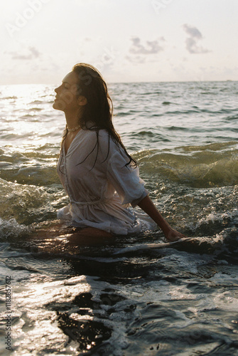 A beautiful young woman in a white dress, immersed in the sea