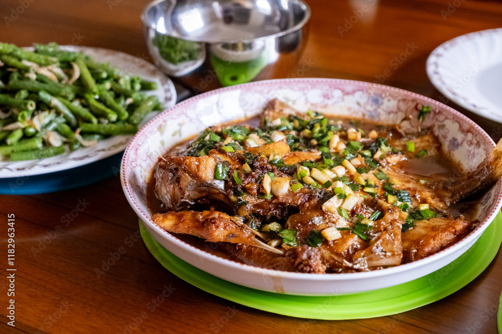 A Chinese home-cooked meal featuring a fish smothered in rich soy sauce, garnished with chopped scallions, and served with a side dish of stir-fried green beans. A Chinese home-cooked meal featuring a fish smothered in rich soy sauce, garnished with chopped scallions, and served with a side dish of stir-fried green beans.