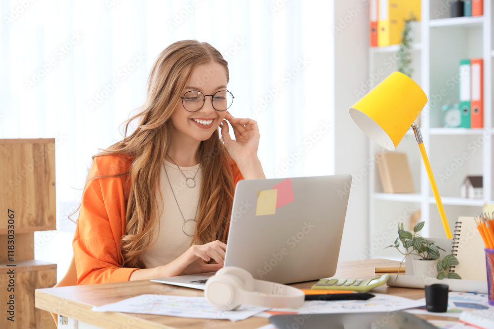 © Pixel-Shot - Female web designer working with laptop at table in office