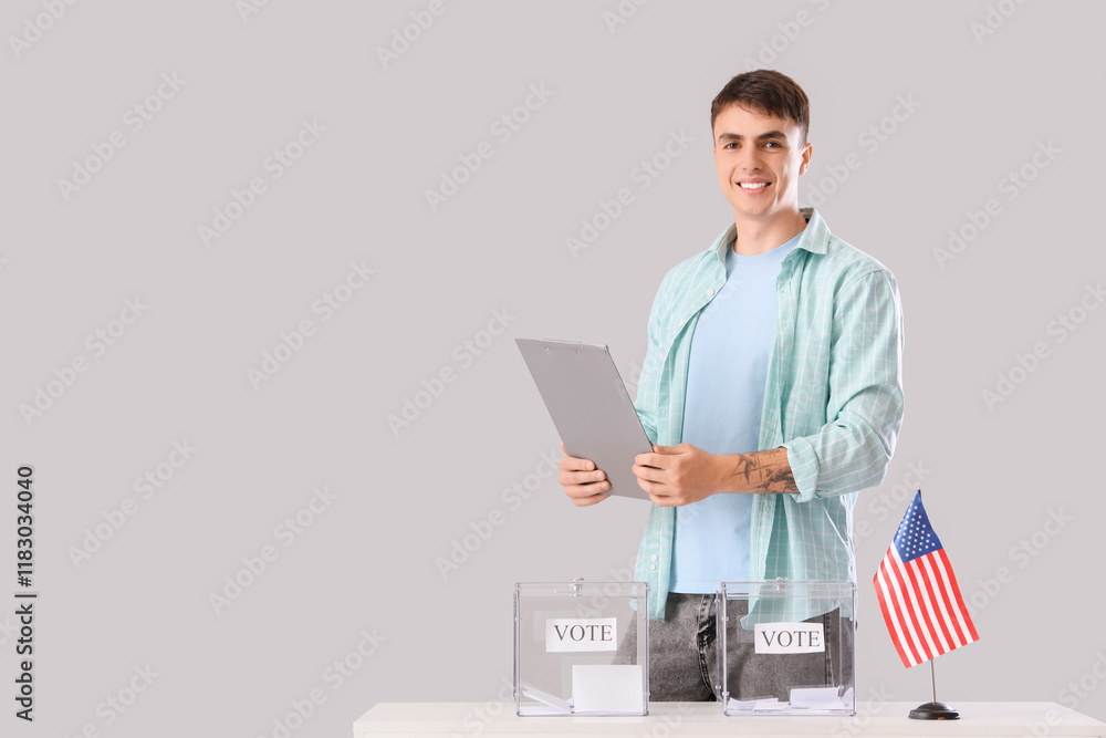 Voting young man with clipboard near ballot box and USA flag at table on light background Voting young man with clipboard near ballot box and USA flag at table on light background
