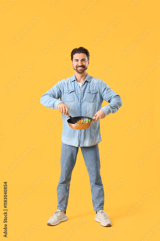 Handsome bearded man frying vegetables on yellow background Handsome bearded man frying vegetables on yellow background