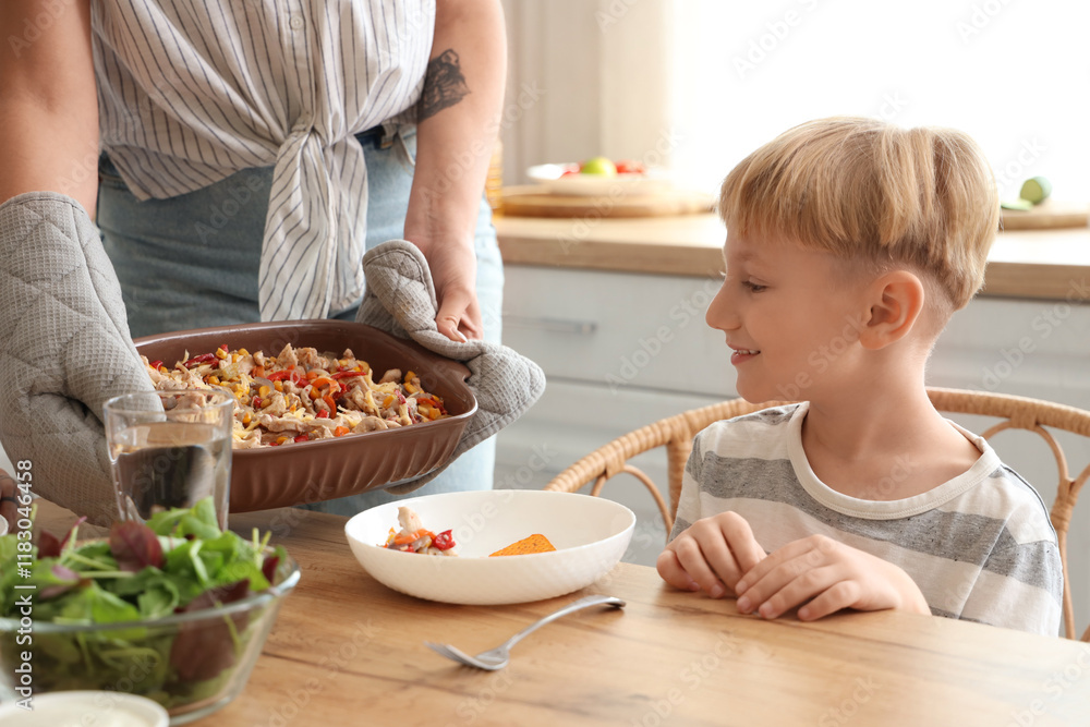 Young woman putting Fajita on table at dinner with her little son in kitchen Young woman putting Fajita on table at dinner with her little son in kitchen