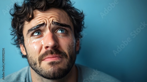 A man with an expression of deep sadness, eyes filled with tears and mouth trembling, against a soft blue background photo