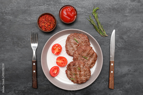 Fototapeta Naklejka Na Ścianę i Meble -  Plate with tasty meat cutlets, cut tomatoes, rosemary, bowl of ketchup and cutlery on black grunge background
