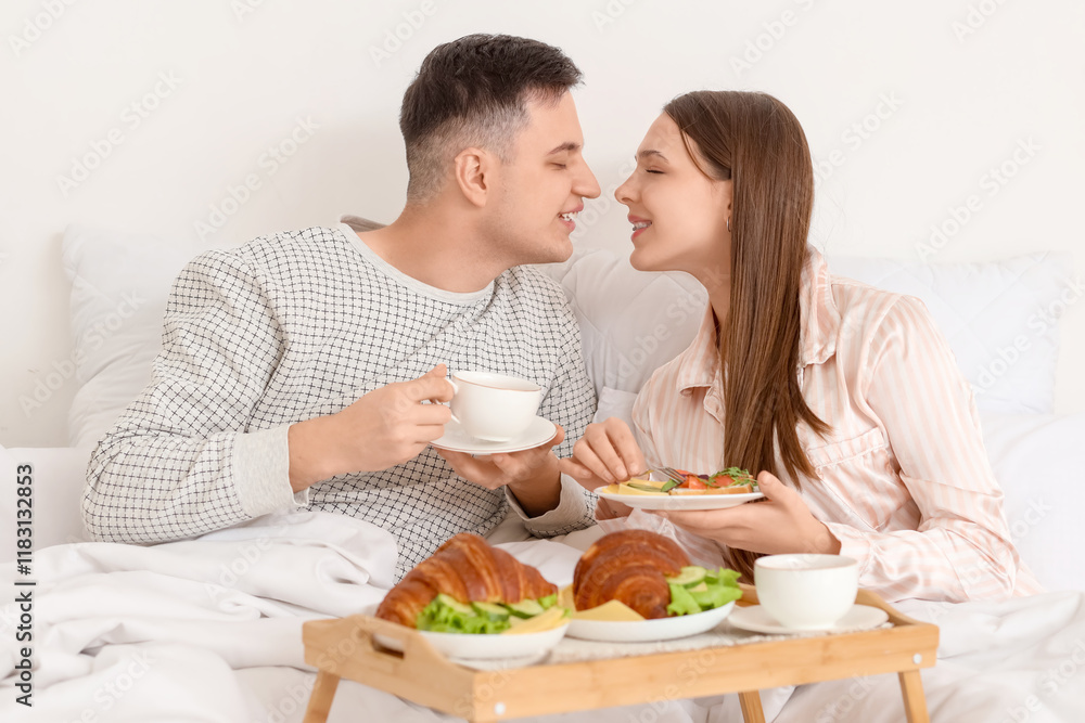 Kissing young couple having breakfast in bed at home Kissing young couple having breakfast in bed at home
