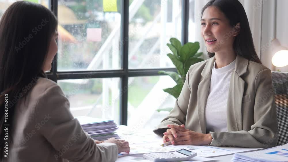 Two women are sitting at a table, one of them smiling. They are talking to each other Two women are sitting at a table, one of them smiling. They are talking to each other